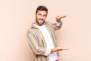 Delikanlı iki eli yanda olan bir objeyi tutuyor fotokopi alanı, bir nesneyi gösteriyor, sunuyor ya da reklamını yapıyor.