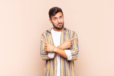 Genç adam şaşkın ve şaşkın görünüyor, güvensiz ve şüpheyle zıt yönleri işaret ediyor.