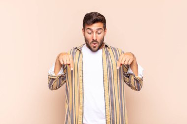 İki eliyle aşağıya bakan ağzı açık genç bir adam, şaşkın, şaşkın ve şaşırmış görünüyor.