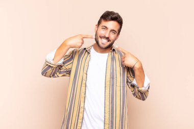 Genç adam kendinden emin bir şekilde gülümseyerek kendi geniş gülüşünü, pozitif, rahat, tatmin olmuş tavrını gösteriyor.