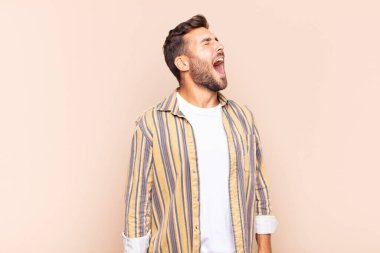 Genç adam öfkeyle bağırıyor, agresif bir şekilde bağırıyor, stresli ve sinirli görünüyor.