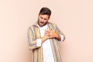 Genç adam üzgün, yaralı ve kalbi kırık görünüyor, iki elini de kalbe yakın tutuyor, ağlıyor ve bunalımda.