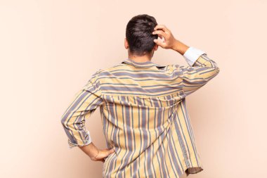 Genç adam bilgisiz ve kafası karışık, bir çözüm düşünüyor, eli kalçasında, diğeri kafasında, dikiz aynasından.