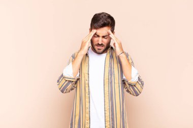 Genç adam stresli ve hayal kırıklığına uğramış görünüyor, baskı altında çalışıyor, başı ağrıyor ve sorunlarla boğuşuyor.