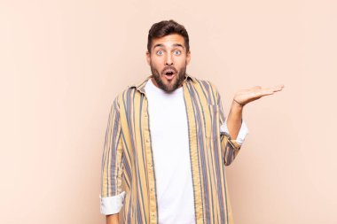 Genç adam şaşırmış ve şok olmuş görünüyor, çenesi düşmüş bir nesneyi elinde açık bir elle tutuyor.