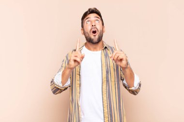 Genç adam şaşırmış, şaşırmış ve ağzı açık bir şekilde iki eliyle uzayı göstererek uzayı kopyalıyor.