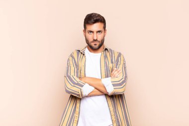 Genç adam mutsuz ve hayal kırıklığına uğramış, ciddi görünüyor, sinirlenmiş ve kollarını kavuşturmuş.