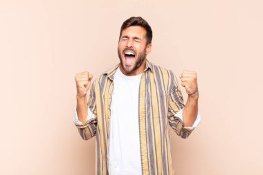 Genç adam son derece mutlu ve şaşırmış görünüyor, başarıyı kutluyor, bağırıyor ve zıplıyor.