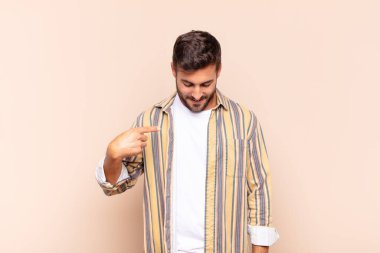 Genç adam neşeyle gülümsüyor, yere bakıyor ve göğsüne işaret ediyor.