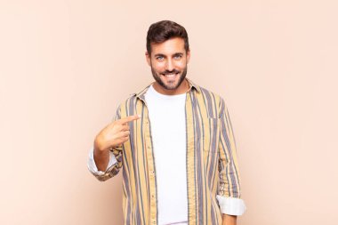 Genç adam gururlu, kendinden emin ve mutlu görünüyor, gülümsüyor ve kendini işaret ediyor veya bir numaralı işareti yapıyor.