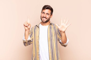 Genç adam gülümsüyor ve arkadaş canlısı görünüyor, 6 ya da 6 numarayı gösteriyor, elleri önde, geriye doğru sayıyor.