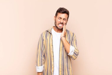 Yanak tutan ve acı çeken diş ağrısı çeken genç adam hasta, sefil ve mutsuz hisseden, dişçi arayan.