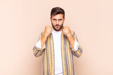 Genç adam kendinden emin, sinirli, güçlü ve agresif görünüyor. Yumrukları boks pozisyonunda dövüşmeye hazır.