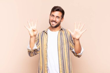 Genç adam gülümsüyor ve dost canlısı görünüyor, 9 ya da 9 numarayı gösteriyor, eli önde, geriye doğru sayıyor.