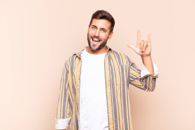 Genç adam mutlu, eğlenceli, kendinden emin, pozitif ve asi hissediyor, elle kaya veya heavy metal işareti yapıyor.