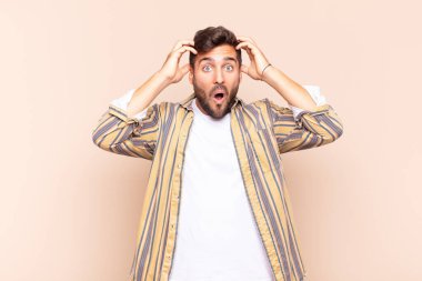 Genç adam heyecanlı ve şaşırmış görünüyor, ağzı açık, elleri başının üstünde, şanslı bir kazanan gibi hissediyor.