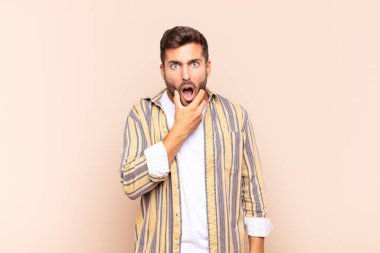 Ağzı ve gözleri açık, eli çenesinde olan genç bir adam, nahoş bir şekilde şokta, ne ya da vay canına diyor.