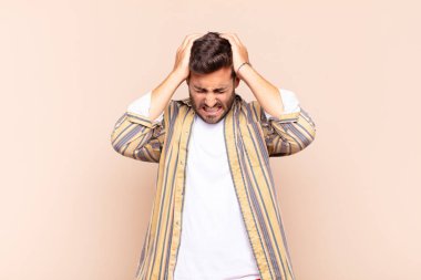 Genç adam kendini stresli ve hayal kırıklığına uğramış hissediyor, ellerinizi havaya kaldırıyor, yorgun, mutsuz ve migren ağrısı çekiyor.