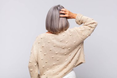 Gri saçlı kadın düşünüyor ya da şüphe ediyor, kafasını kaşıyor, kafası karışık ve kafası karışık, arkaya ya da arkaya bakıyor.