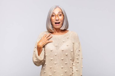 Gri saçlı kadın şaşkın, şaşkın ve şaşırmış hissediyor, elleri göğsünde ve ağzı açık, kim olduğumu söylüyor, ben?