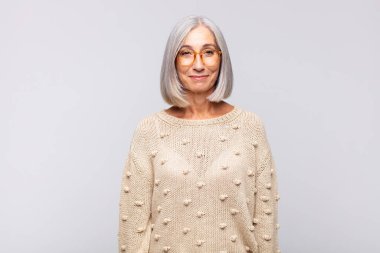 Gri saçlı kadın pozitif ve kendinden emin gülümsüyor. Tatmin olmuş, arkadaş canlısı ve mutlu görünüyor.