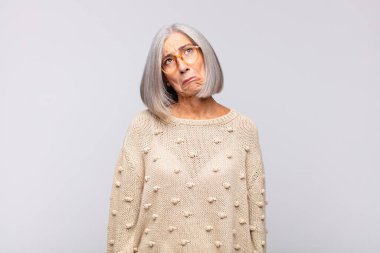 Gri saçlı, üzgün ve mızmız bir kadın. Mutsuz bir bakışla ağlıyor. Olumsuz ve hayal kırıklığına uğramış bir tavırla ağlıyor.