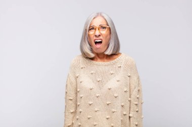 Gri saçlı kadın korkmuş ve şok olmuş hissediyor, ağzı açık şaşkınlık içinde.