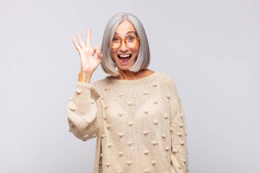 Gri saçlı kadın kendini başarılı ve tatmin olmuş hissediyor, ağzı açık gülümsüyor, elle işaret veriyor.