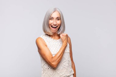 Gri saçlı kadın mutlu, pozitif ve başarılı hissediyor, meydan okumayla karşılaştığında motive oluyor ya da iyi sonuçları kutluyor.