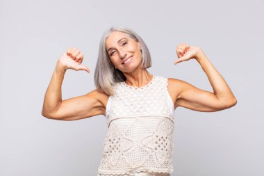 Gri saçlı kadın gururlu, kibirli ve kendinden emin, tatmin olmuş ve başarılı görünüyor, kendini işaret ediyor.