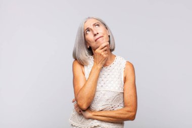 Gri saçlı kadın düşünüyor, kuşkulu ve şaşkın hissediyor, farklı seçeneklerle, hangi kararı vereceğini merak ediyor.