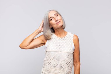 Gri saçlı kadın neşeli ve sıradan bir şekilde gülümsüyor, olumlu, mutlu ve kendinden emin bir bakışla yumruk yumruğa.