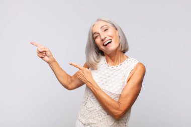 Gri saçlı, neşeli ve şaşırmış bir kadın. Şok olmuş bir ifadeyle gülümsüyor.