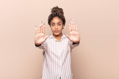 Genç afro kadın ciddi, mutsuz, kızgın ve hoşnutsuz görünüyor. Girmeyi yasaklıyor ya da her iki avuçta da dur diyor.