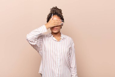 Genç afro kadın tek eliyle gözlerini kapatıyor korkmuş ya da endişeli hissediyor, merak ediyor ya da körü körüne bir sürpriz bekliyor.