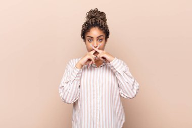 Genç afro kadın ciddi ve hoşnutsuz görünüyor. İki parmağının önde olması reddedilerek sessizlik istiyor.