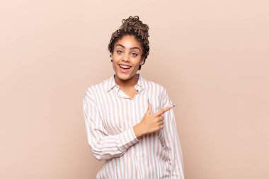 Genç afro kadın heyecanlı ve şaşırmış görünüyor. Yana ve yukarı doğru uzayı gösteriyor.