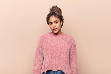 Genç afro kadın neşeyle gülümsüyor, yere bakıyor ve göğsüne işaret ediyor.