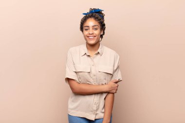 Genç afro kadın utangaç ve neşeli bir şekilde gülüyor, arkadaş canlısı ve olumlu ama güvensiz bir tavırla