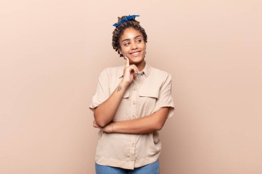 Genç afro kadın mutlu bir şekilde gülümsüyor ve hayal kuruyor ya da şüphe ediyor, yan tarafa bakıyor.