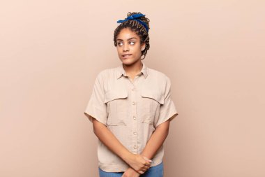 Genç afro kadın şüphe ediyor ya da düşünüyor, dudağını ısırıyor ve kendini güvensiz ve gergin hissediyor, kenarda yer arıyor.