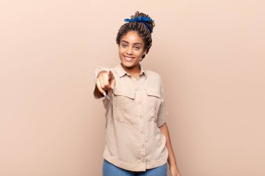 Genç afro kadın kameraya tatmin olmuş, kendinden emin, dost canlısı bir gülümsemeyle bakıyor ve seni seçiyor.