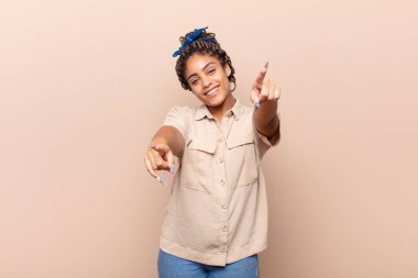 Genç afro kadın mutlu ve kendinden emin, kamerayı iki eliyle gösteriyor ve gülüyor, seni seçiyor.
