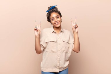 Genç afro kadın gülümsüyor ve mutlu görünüyor, arkadaş canlısı ve memnun, işaret ediyor zafer ya da barış iki elle