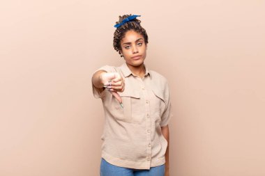 Genç afro kadın kızgın, sinirli, hayal kırıklığına uğramış ya da hoşnutsuz, ciddi bir bakışla başparmağını kaldırıyor.