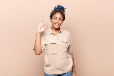 Genç afro kadın mutlu, rahat ve tatmin olmuş hissediyor. Onayını iyi bir hareketle gösteriyor. Gülümsüyor.