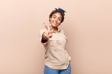 Genç afro kadın gülümsüyor ve mutlu görünüyor, kaygısız ve pozitif, zafer ya da barışı simgeliyor.