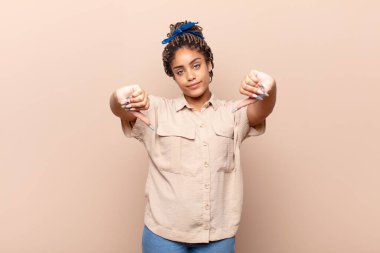 Genç afro kadın üzgün, hayal kırıklığına uğramış ya da kızgın görünüyor, anlaşmazlık içinde başparmaklarını gösteriyor, hayal kırıklığına uğramış hissediyor.