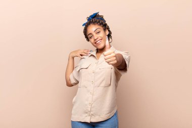 Genç afro kadın gururlu, kaygısız, kendinden emin ve mutlu, olumlu gülümsüyor.