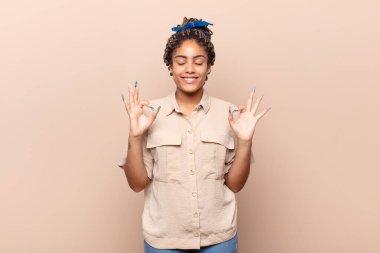 Genç afro kadın konsantre olmuş ve meditasyon yapıyor, kendini tatmin olmuş ve rahatlamış hissediyor, düşünüyor ya da bir seçim yapıyor.